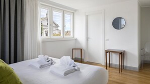 Ein Hotelzimmer mit einem Bett, einem Fenster mit Vorhängen, einem runden Spiegel und einem kleinen Holztisch.