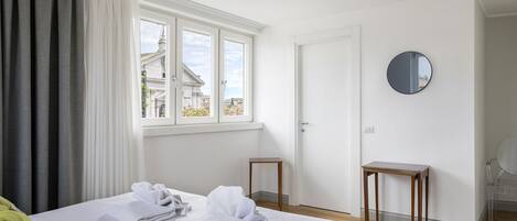 A hotel room with a bed, a window with curtains, a round mirror, and a small wooden table.