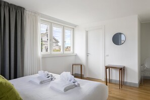 A hotel room with a bed, a window with curtains, a round mirror, and a small wooden table. - iFlat | Penthouse Rome Capitol (Roma)