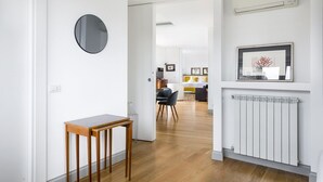 Ein Korridor mit einem Holztisch, einem runden Spiegel, einem Heizkörper und einem gerahmten Bild an der Wand.