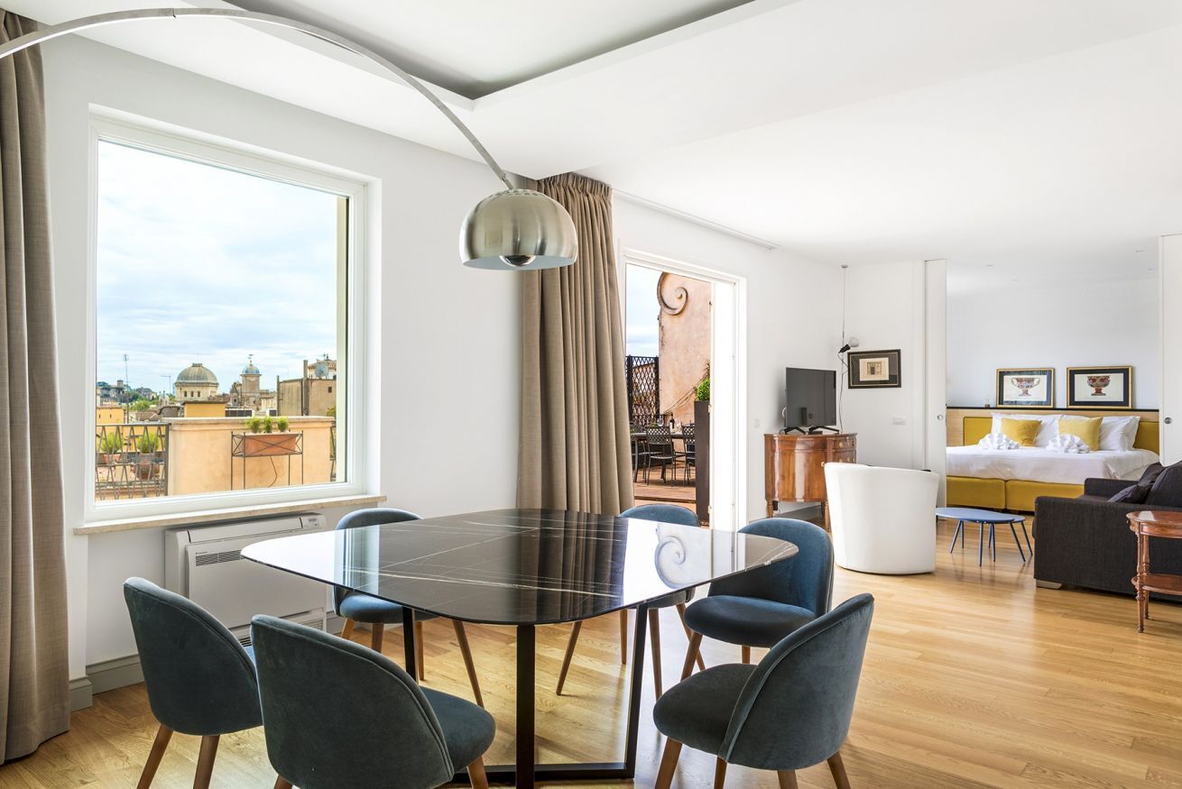Ein modernes Wohnzimmer mit Esstisch, Stühlen, einer Couch, einem Fernseher und einem großen Fenster mit Blick auf Gebäude.
