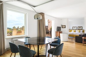 A modern living room with a dining table, chairs, a sofa, a TV, and a large window with a view of buildings. - iFlat | Penthouse Rome Capitol (Roma)