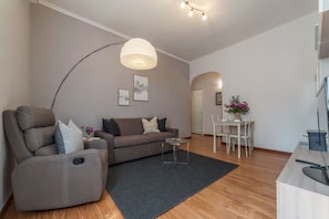 A modern living room with a sofa, a recliner, a dining table, and a kitchen area.
