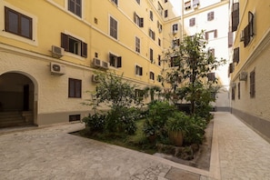 A courtyard with a central garden, buildings with multiple windows, and a stone-paved ground.