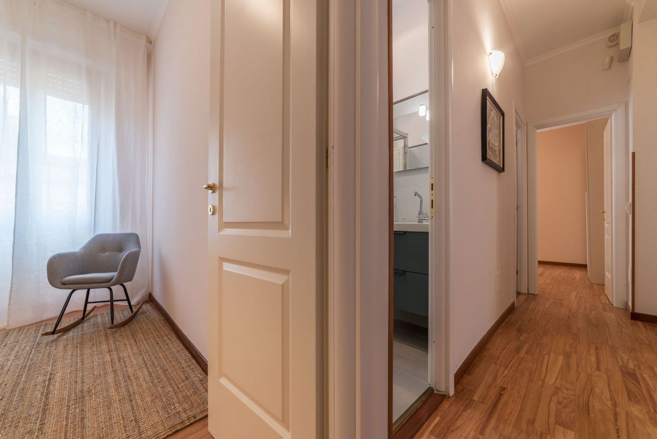 A hallway with a door leading to a bathroom, a chair, and a light fixture.