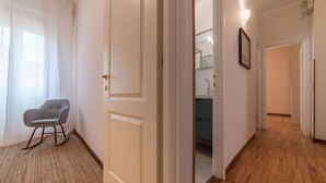 A hallway with a door leading to a bathroom, a chair, and a light fixture. - iFlat | Augustus Suite near Saint Peter (Roma)