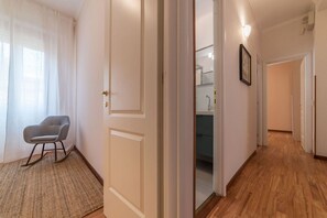 A hallway with a door leading to a bathroom, a chair, and a light fixture. - iFlat | Augustus Suite near Saint Peter (Roma)
