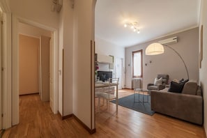 A modern living room with a sofa, a dining table, and a TV. There is a hallway leading to another room.
