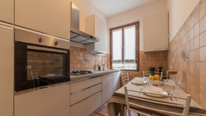 A modern kitchen with a built-in oven, stainless steel range hood, and a dining area with a table set for two. - iFlat | Augustus Suite near Saint Peter (Roma)