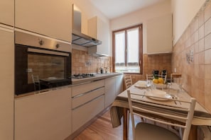 A modern kitchen with a built-in oven, stainless steel range hood, and a dining area with a table set for two. - iFlat | Augustus Suite near Saint Peter (Roma)