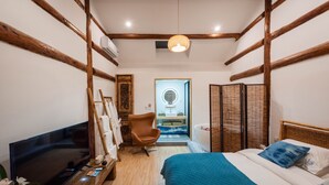 A bedroom with a bed, a television, a chair, a mirror, and a bathroom visible through an open door.