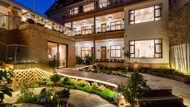 A multi-story hotel with a wooden facade, outdoor wooden deck, and potted plants.
