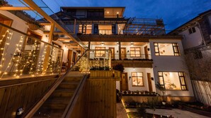 A multi-story house with a wooden staircase, balconies with plants, and string lights.