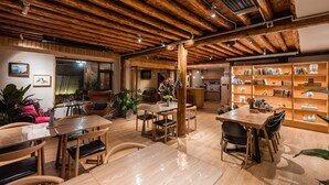 A spacious room with wooden floors, a dining area with a wooden table and chairs, a bookshelf with books and decorative items, and a kitchen area in the background.
