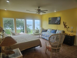 A bedroom with a bed, a chair, a television, and a view of the outdoors.