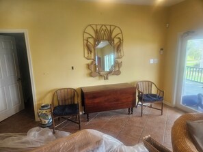 A room with a large mirror, a wooden dresser, two wicker chairs, and a tiled floor.