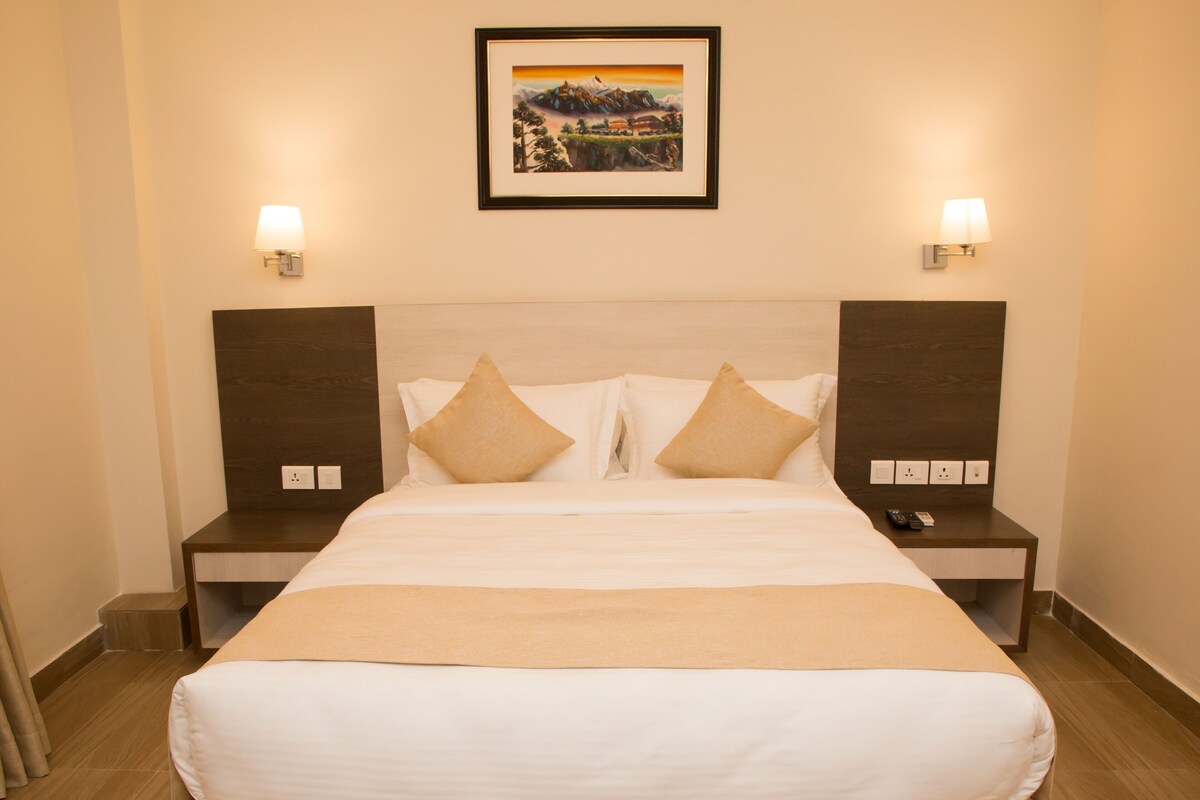A hotel room with a large bed, two bedside tables, a nightstand, a framed picture on the wall, and wall-mounted lamps.