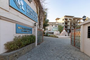 Una entrada con puerta de reja a un edificio residencial, con un letrero que dice "Sarovar Residency Service Apartment Hotel" y un letrero más pequeño que indica "Meena Cottages".