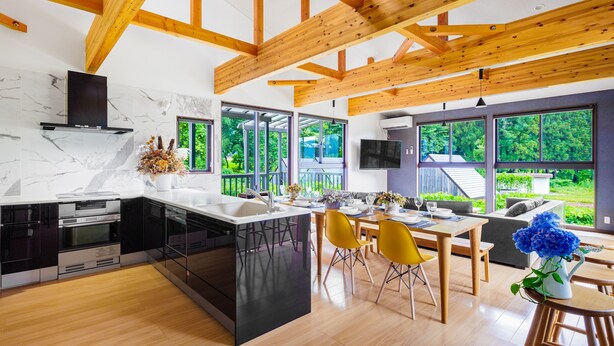 Una cocina moderna con una isla central, vigas de madera y ventanas amplias que ofrecen vistas al verdor.