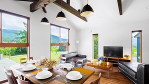 Un salón amplio con una mesa de comedor preparada para cuatro personas, un sofá de cuero y un televisor de pantalla plana.