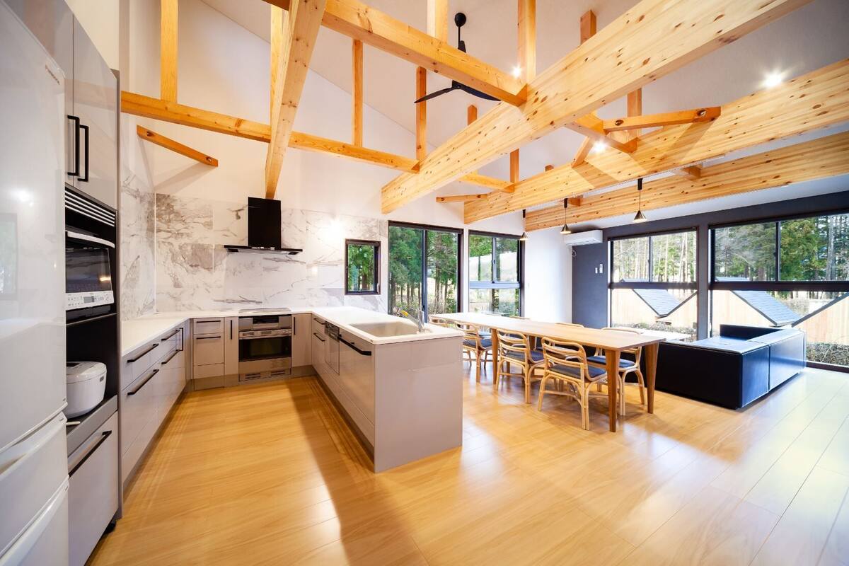 A modern kitchen with wooden beams, a central island, and a dining area with a view of the outdoors.