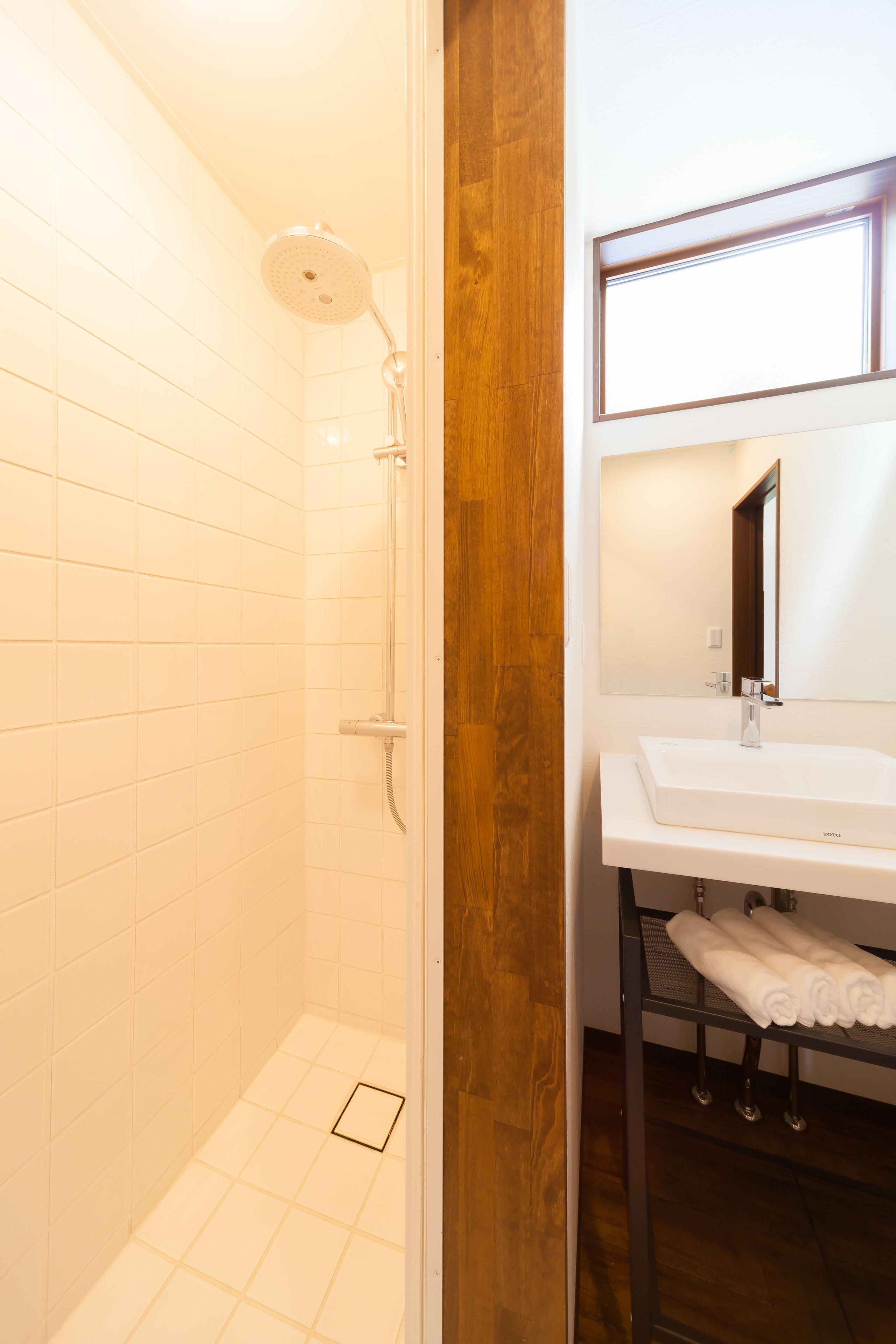 A bathroom with white tiles, a shower, a sink with a mirror, and a wooden accent wall.