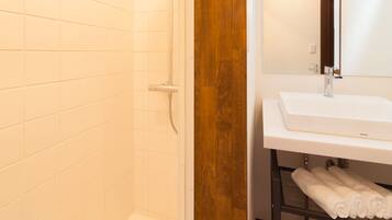 A bathroom with white tiles, a shower, a sink with a mirror, and a wooden accent wall.