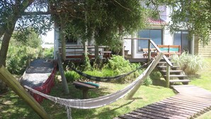 Una hamaca, terraza de madera y zona de estar al aire libre con vista a un edificio al fondo.