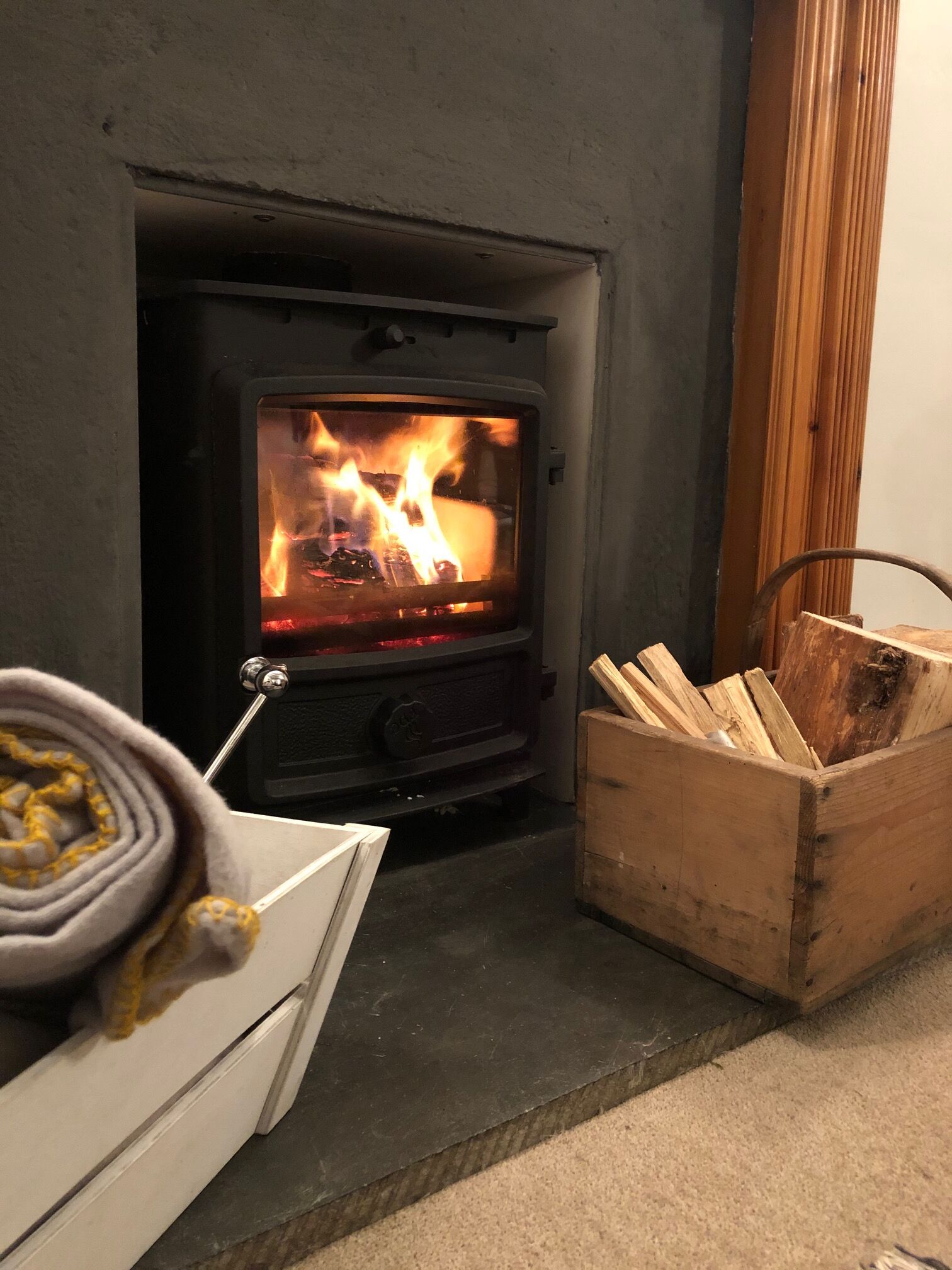 A wood-burning stove with visible flames, a white cabinet, and a wooden box of firewood.