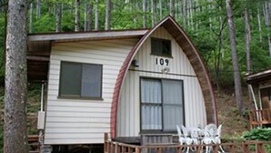 A cabin with a number '109' on the front, a porch with chairs, and a forested backdrop.