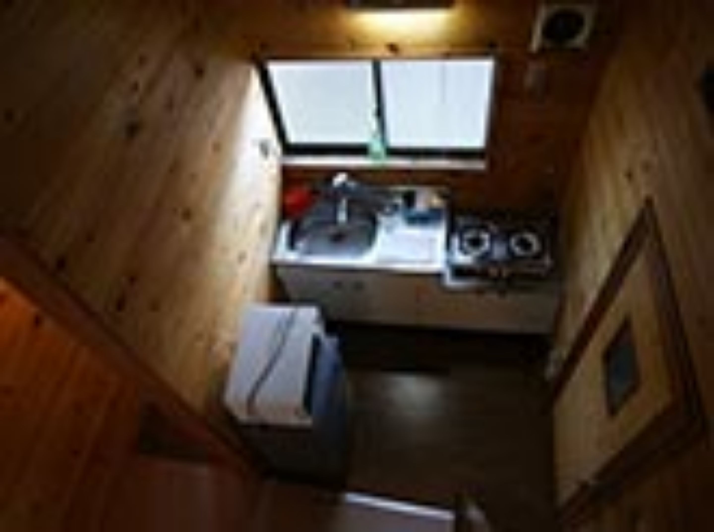 A compact kitchen with wooden walls, a window, and basic amenities.