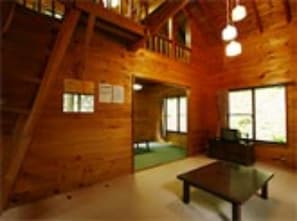 A wooden cabin interior with a staircase, a table, and large windows.