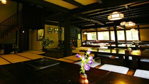 A restaurant interior with wooden beams, large windows, and a table with a vase of flowers.
