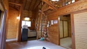 A wooden cabin interior with a central fireplace, wooden beams, and a cozy seating area.