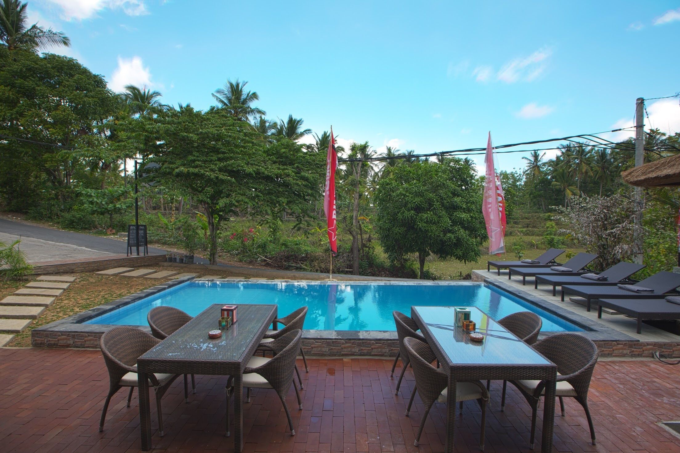 A swimming pool with lounge chairs and a table, surrounded by greenery and palm trees.