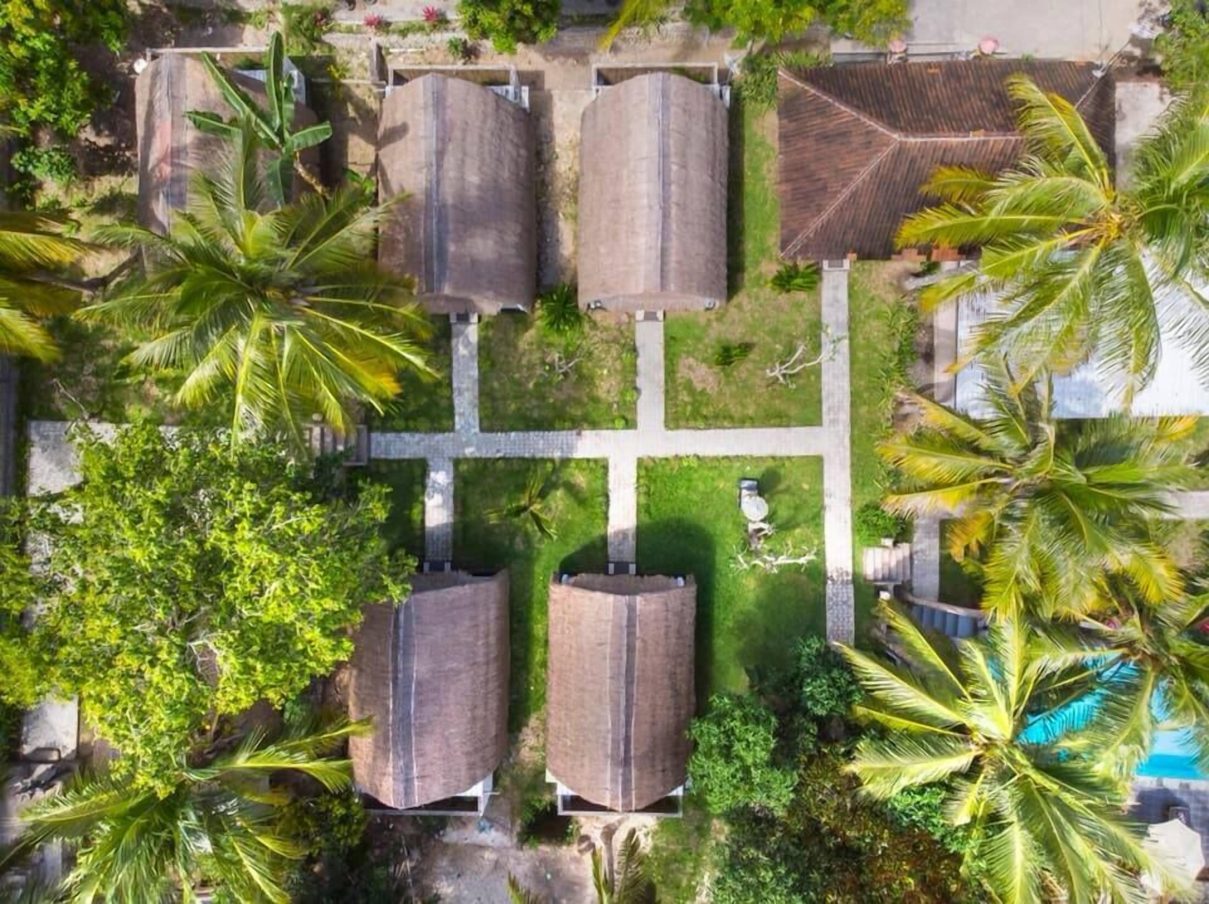 An aerial view of a property with four large cylindrical structures, a central open space, and surrounding greenery including palm trees.