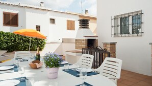 An outdoor dining area with a round table set for two, surrounded by white chairs, a potted plant, and a bottle of champagne. - Villa with swimming-pool and garden.HUTG-015589 (l'Escala)
