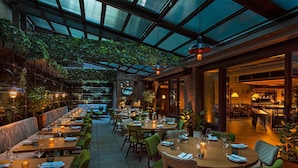 Un restaurante interior con mesas dispuestas para comer, una zona de bar y un techo alto con cubierta de vidrio.