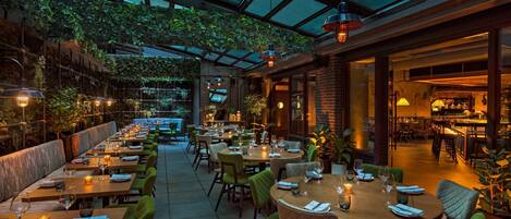 An indoor restaurant with tables set for dining, a bar area, and a high ceiling with a glass roof.