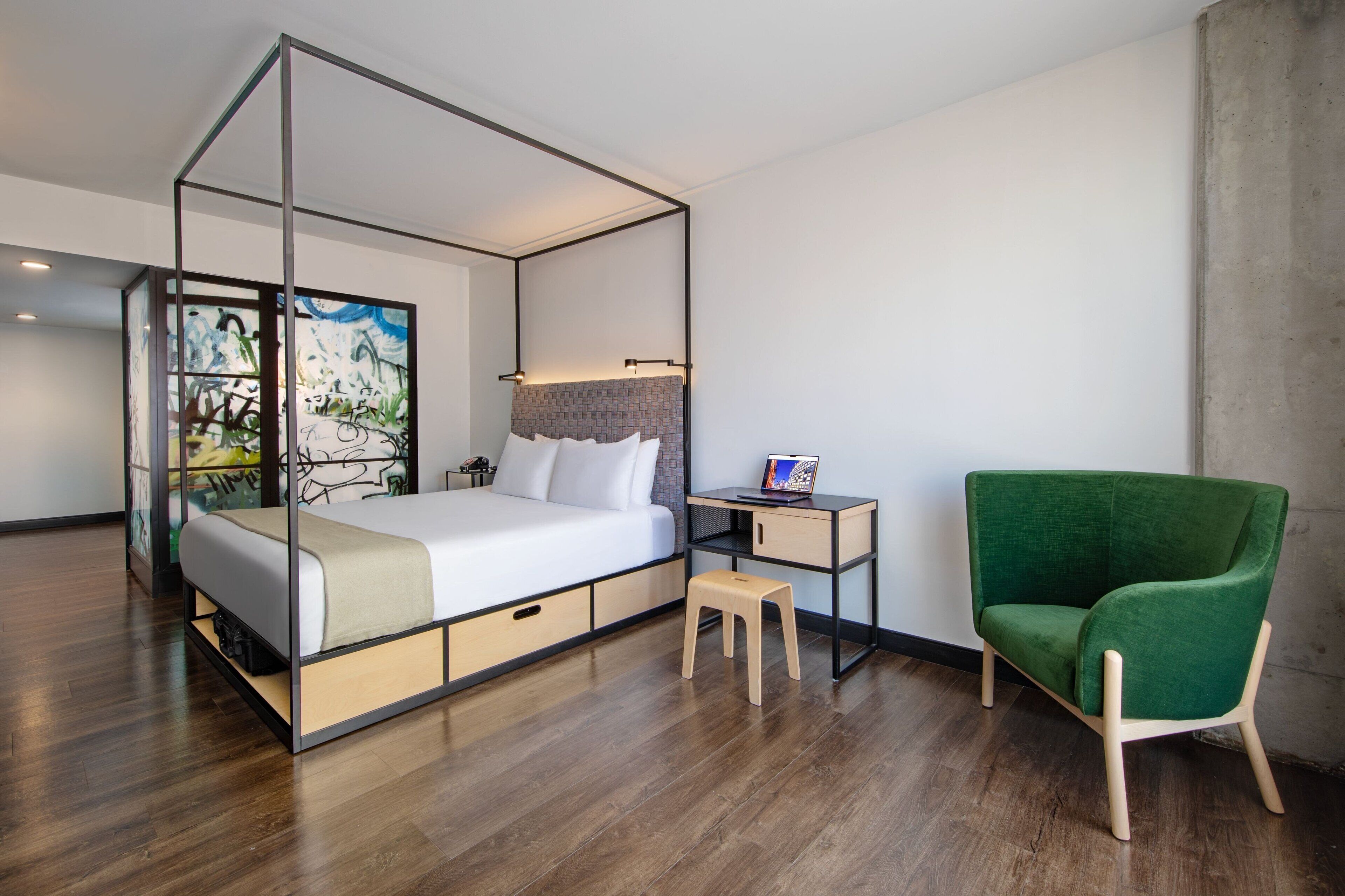 Ein modernes Schlafzimmer mit einem Himmelbett, einem grünen Sessel, einem kleinen Holzschemel und einem Nachttisch mit Lampe.