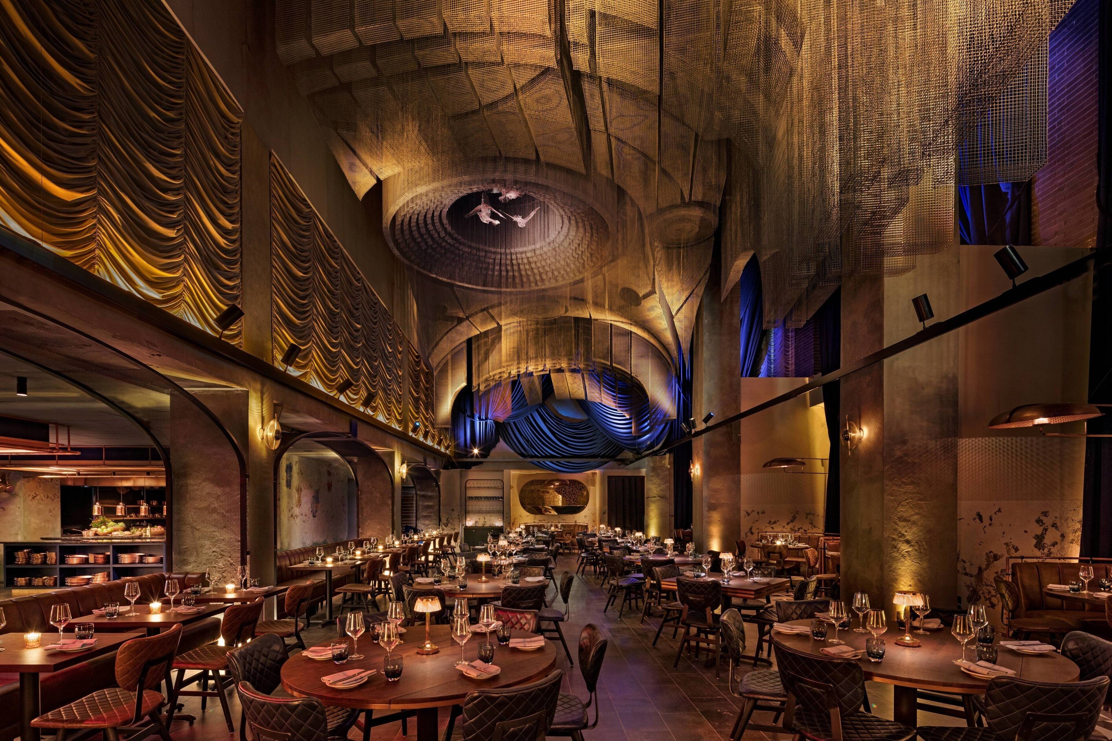 A spacious restaurant with multiple dining areas, high ceilings, and modern lighting fixtures.