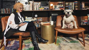 Una persona sentada en una butaca de cuero leyendo un libro, con un perro sentado en otra silla.