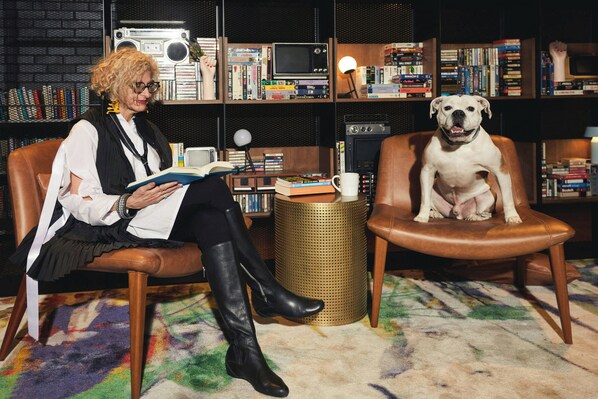 Una persona sentada en una butaca de cuero leyendo un libro, con un perro sentado en otra silla.