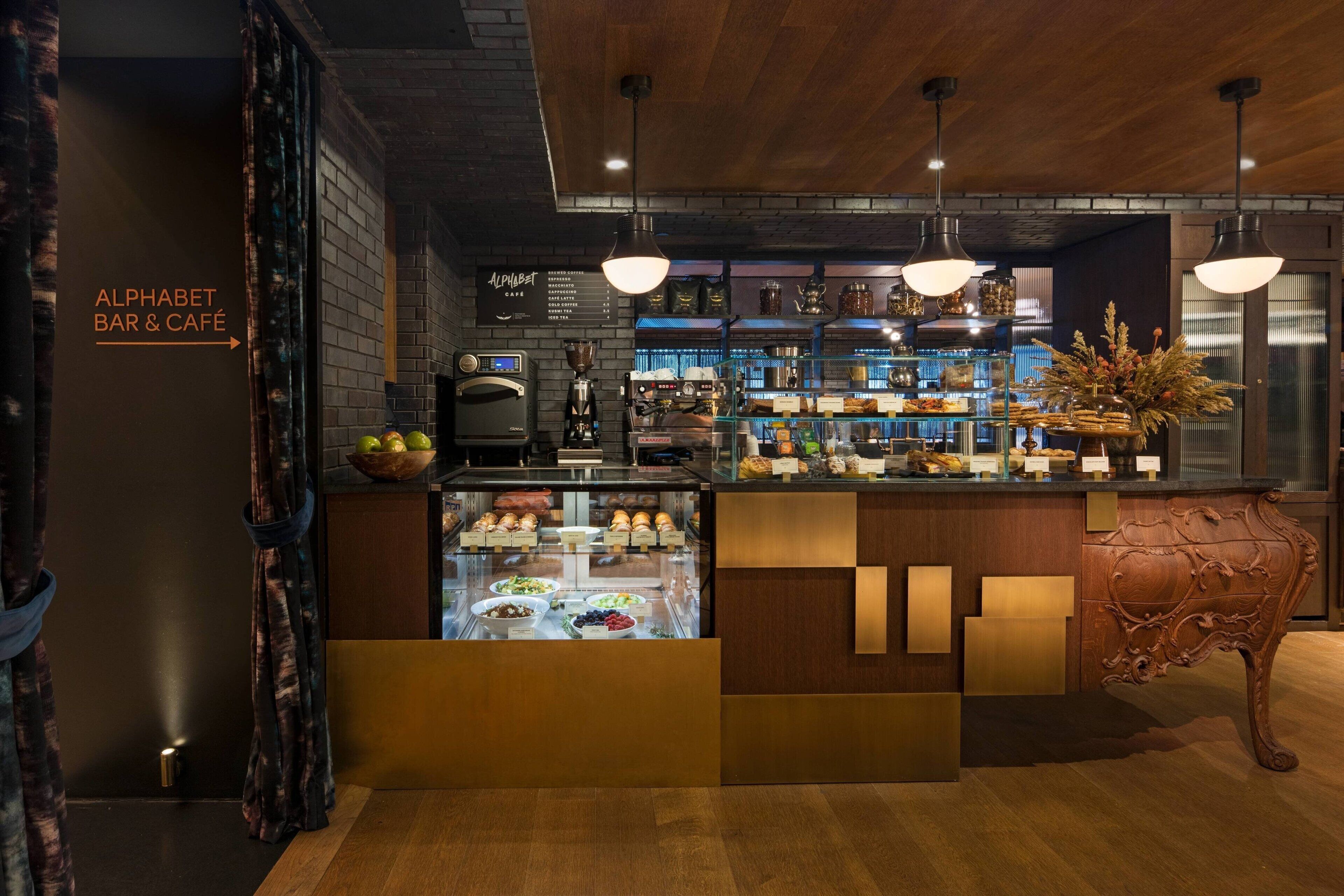 A bar area with a glass display case, wooden counter, and a sign reading "Alphabet Bar & Café".