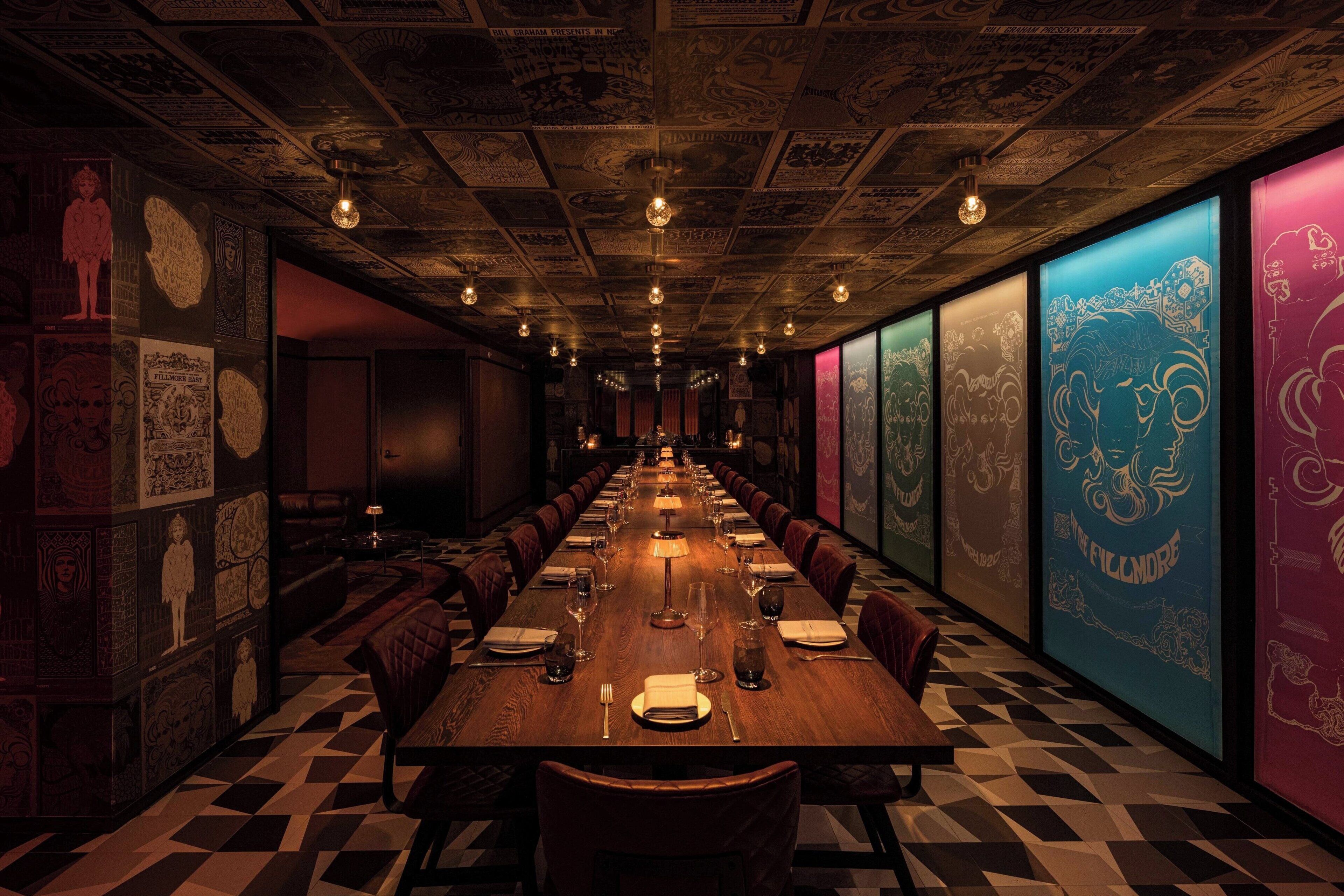 A long, rectangular dining table with chairs, set for a meal. The room has patterned walls and a checkered floor.