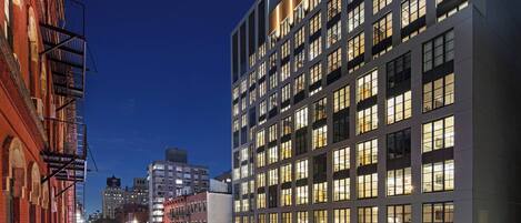 A modern building with multiple floors and large windows, situated along a city street at night.