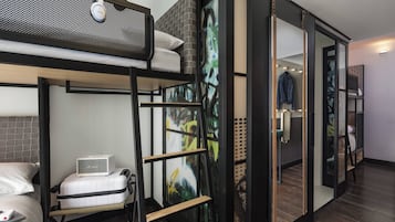 Een moderne hotelkamer met een stapelbed, een Murphy bed, een klein bureau met een laptop en een groot abstract schilderij aan de muur.