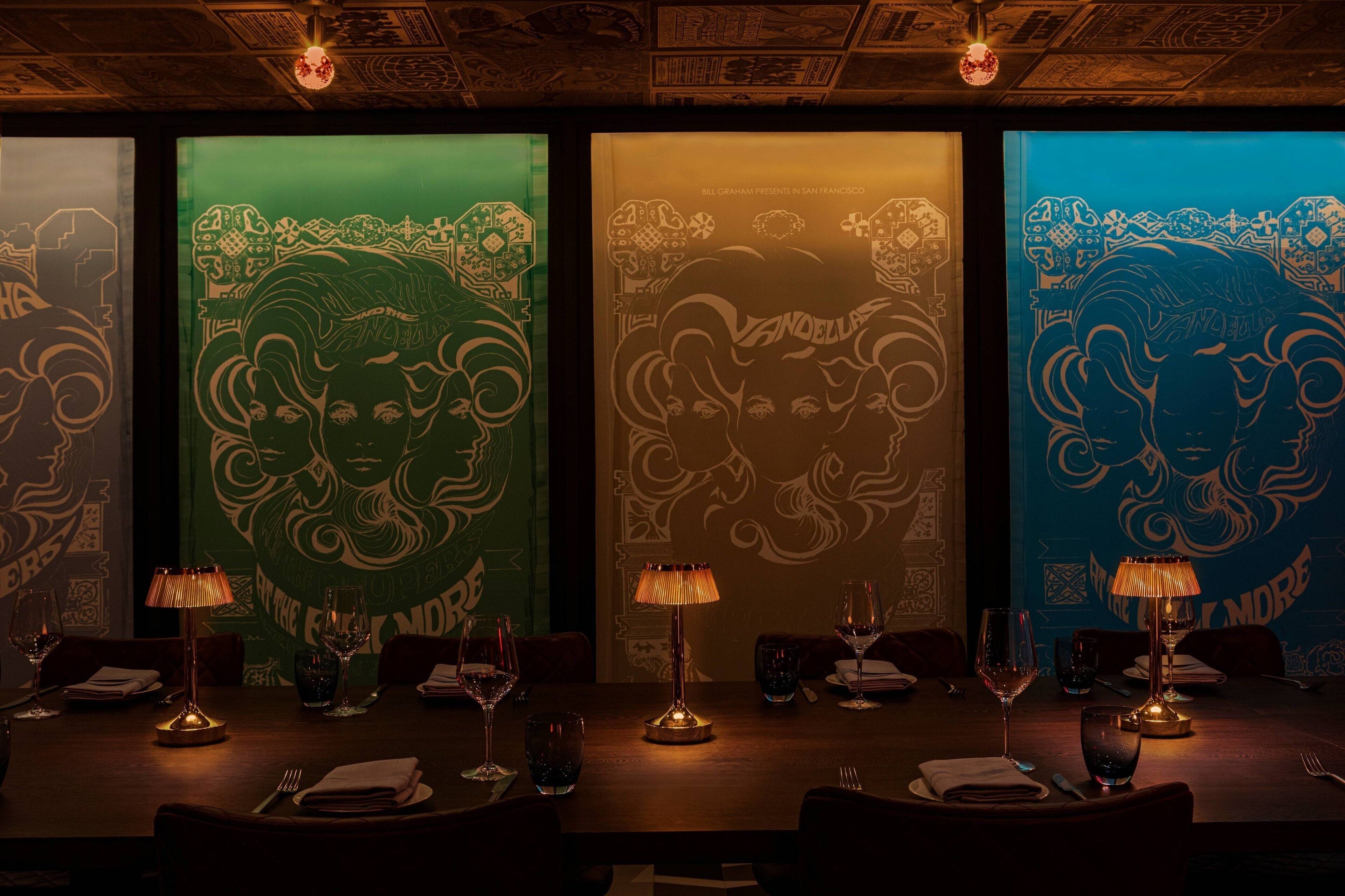 A dimly lit restaurant with a long table set for dining, featuring a unique wall art design and a warm ambiance.