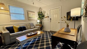A living room with a sofa, coffee table, and a patterned rug. There is a door, a lamp, and a plant in the room. - 1BR NEAR WATER + HEART of CR RIVER-Manatees, Golf, Fish, Beach, Food (Crystal River)