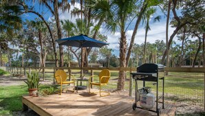 An outdoor deck with wooden flooring, yellow chairs, a blue umbrella, and a barbecue grill. - 1BR NEAR WATER + HEART of CR RIVER-Manatees, Golf, Fish, Beach, Food (Crystal River)